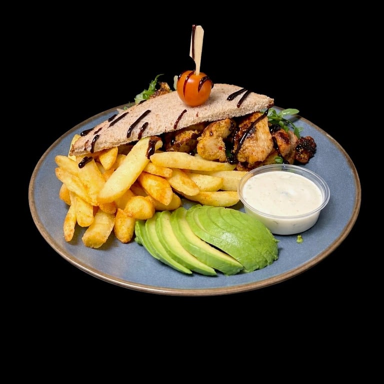Grilled chicken sandwich on blue plate with fries, avocado slices, and white sauce on black background