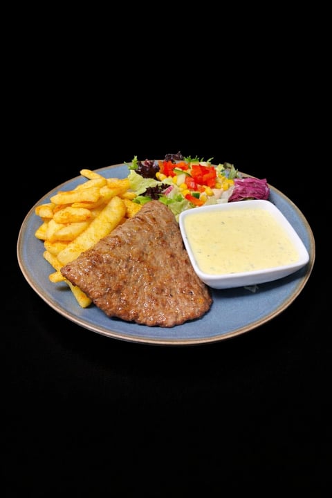 Plated steak dinner with golden fries, fresh vegetable salad, and creamy sauce on blue plate